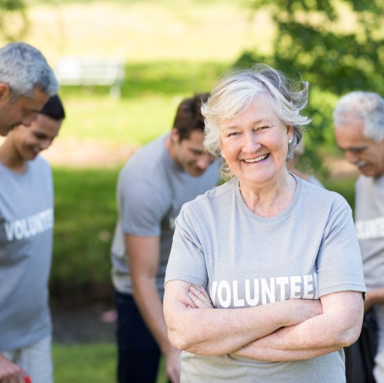 Una mujer mayor con una camiseta que dice "volunteer" sonríe mientras posa junto a un grupo de voluntarios.